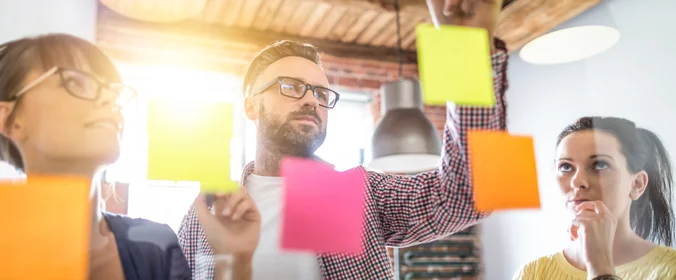 foto de pessoas colando post its em uma lousa transparente